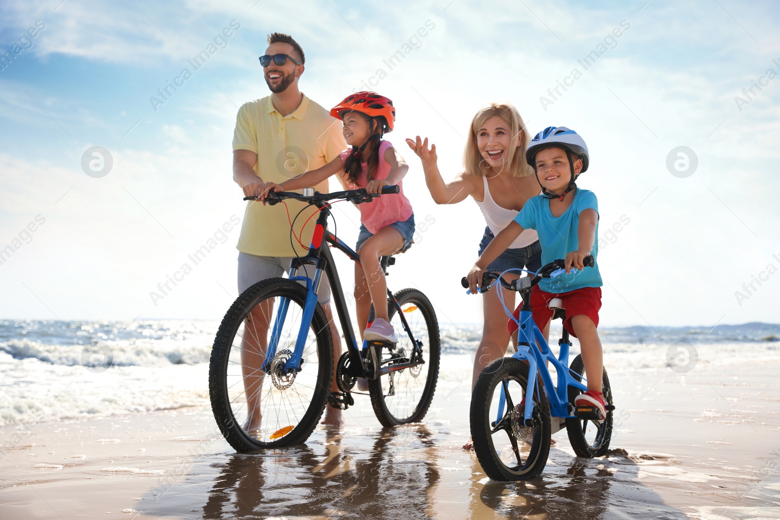 Photo of Happy parents teaching children to ride bicycles on sandy beach near sea