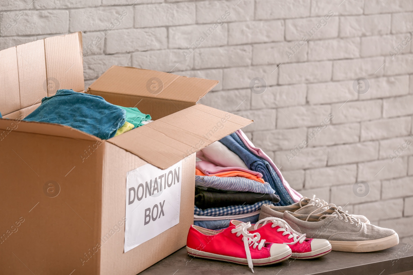 Photo of Donation box with clothes and shoes on table against brick wall