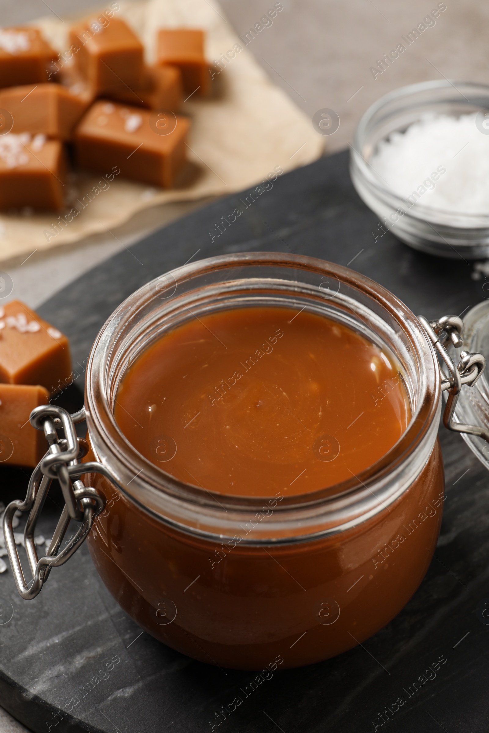 Photo of Tasty salted caramel in glass jar on grey table, closeup