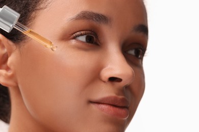 Beautiful woman applying serum onto her face on white background, closeup
