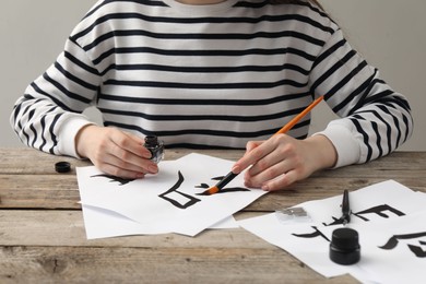 Calligraphy. Woman with brush and inkwell writing hieroglyphs on paper at wooden table, closeup