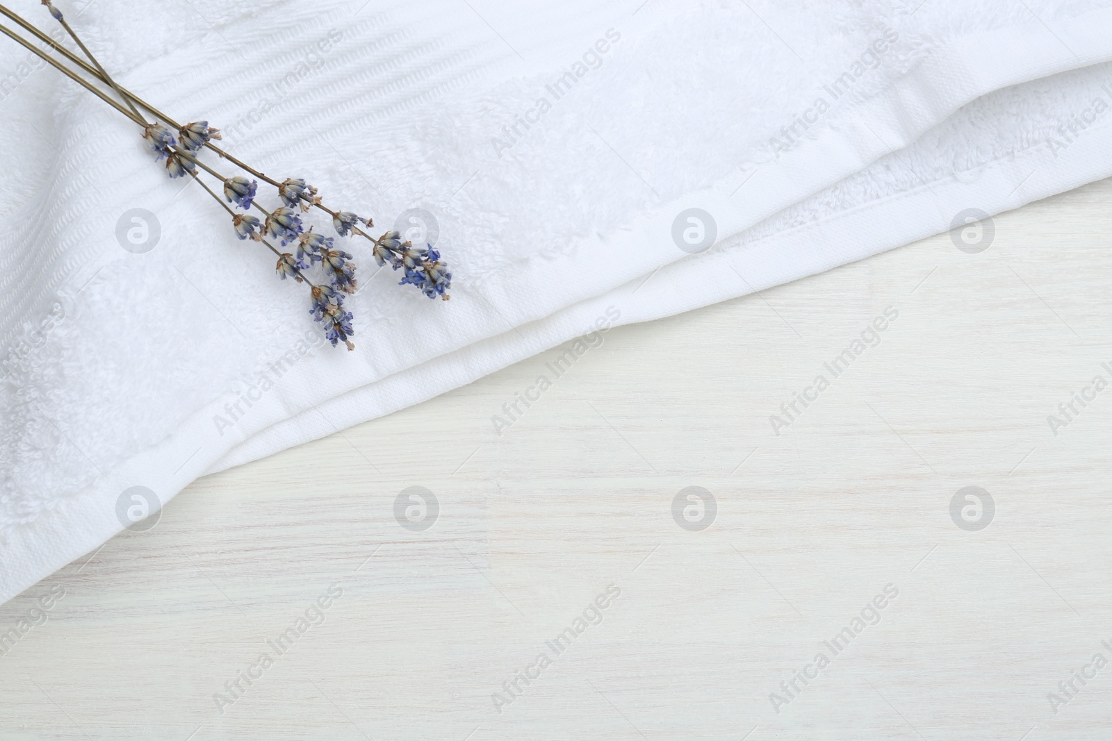 Photo of White terry towel and lavender flowers on light wooden table, top view. Space for text