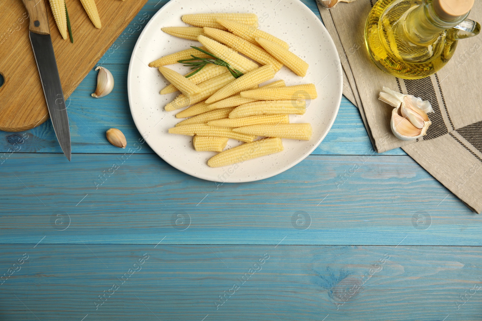 Photo of Fresh baby corn cobs on blue wooden table, flat lay. Space for text