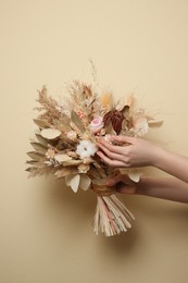 Photo of Woman holding beautiful dried flower bouquet on beige background, closeup