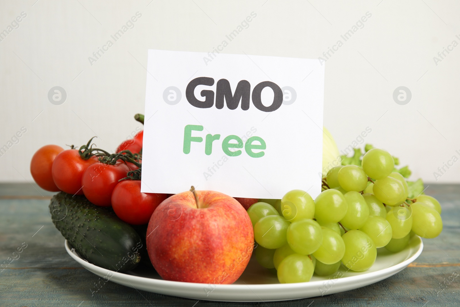 Photo of Fresh fruits, vegetables and card with text GMO Free on light blue wooden table