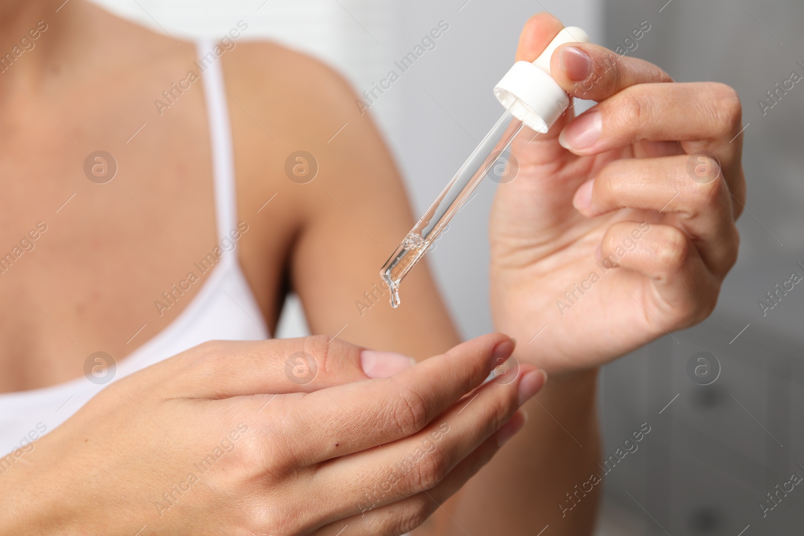 Photo of Woman applying cosmetic serum onto her finger on blurred background, closeup