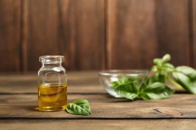 Glass bottle of basil oil and leaf on wooden table. Space for text