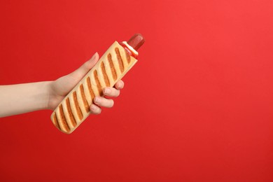 Woman holding delicious french hot dog on red background, closeup. Space for text