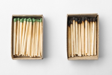 Cardboard boxes with whole and burnt matches on white background, top view