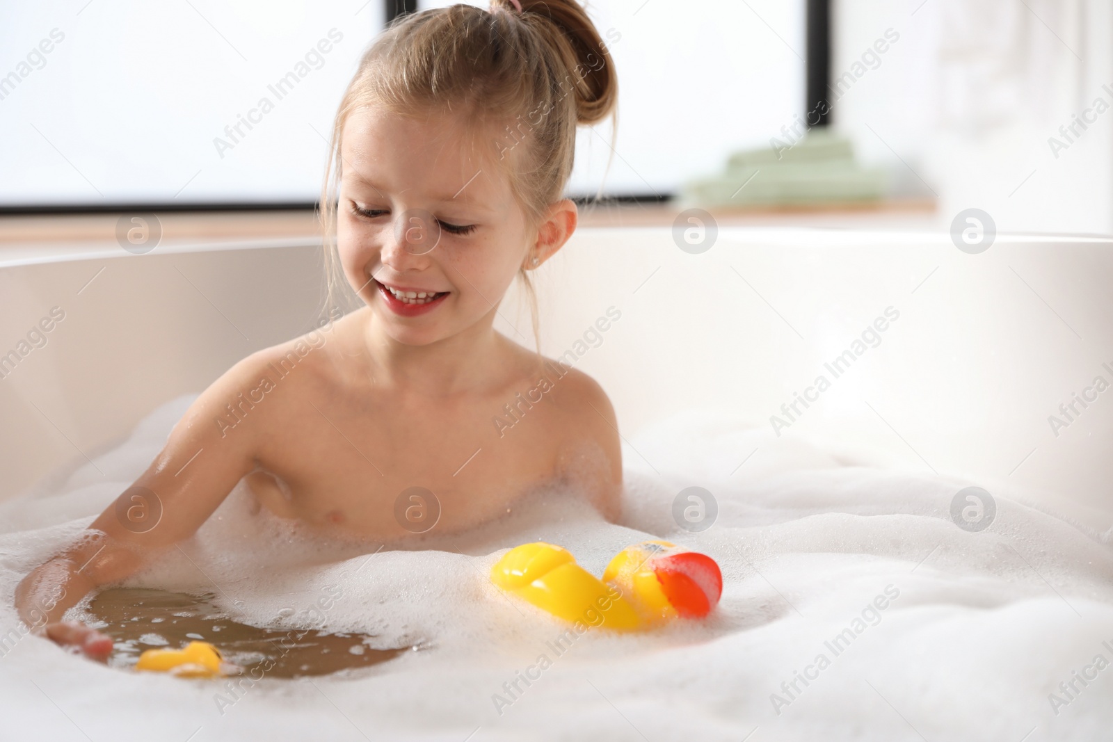 Photo of Cute little girl taking bubble bath at home