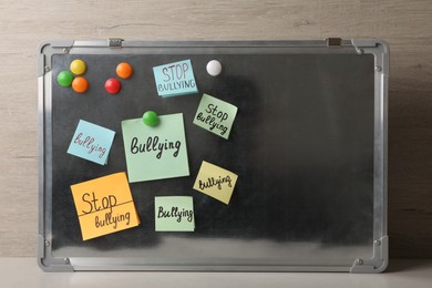 Notes with phrase Stop Bullying attached to board on table near wooden wall