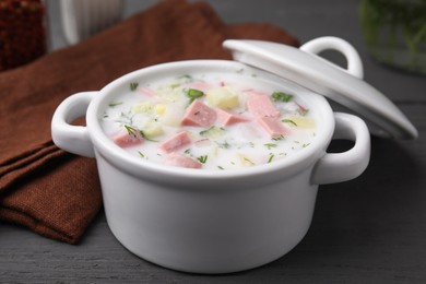 Delicious cold summer soup (okroshka) with boiled sausage in pot on grey wooden table