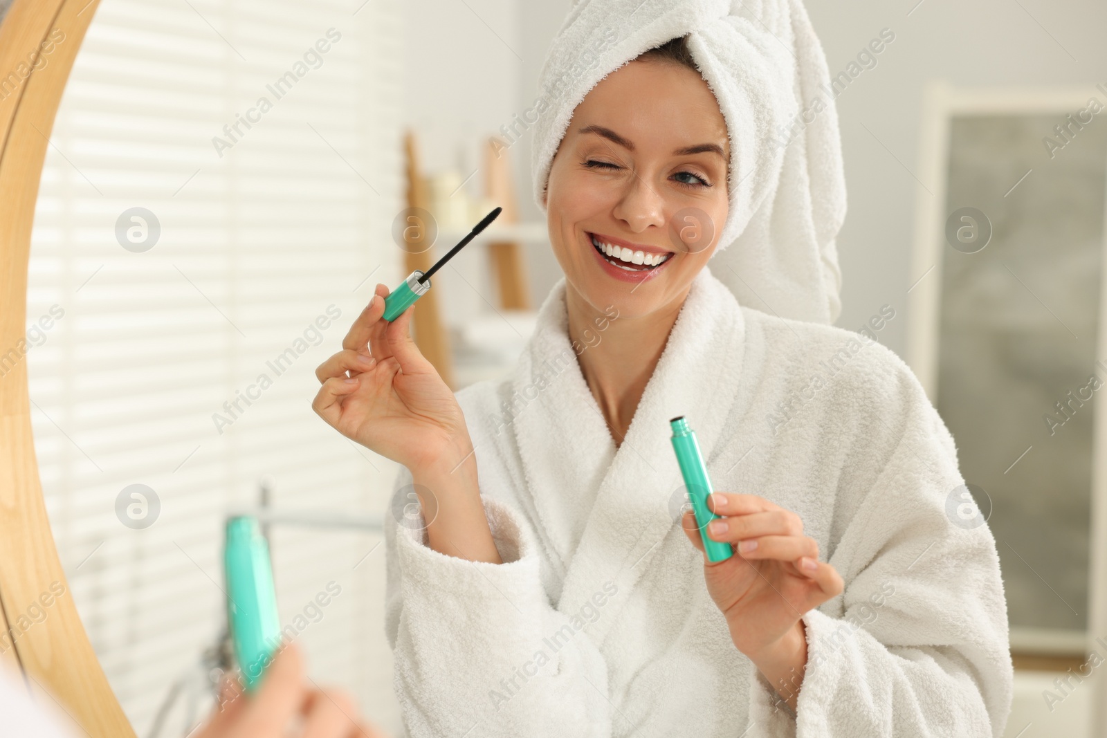 Photo of Beautiful woman applying mascara near mirror in bathroom