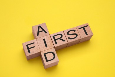 Photo of Words First Aid made of wooden cubes on yellow background, above view