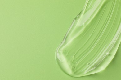 Photo of Smear of clear cosmetic gel on light green background, top view. Space for text
