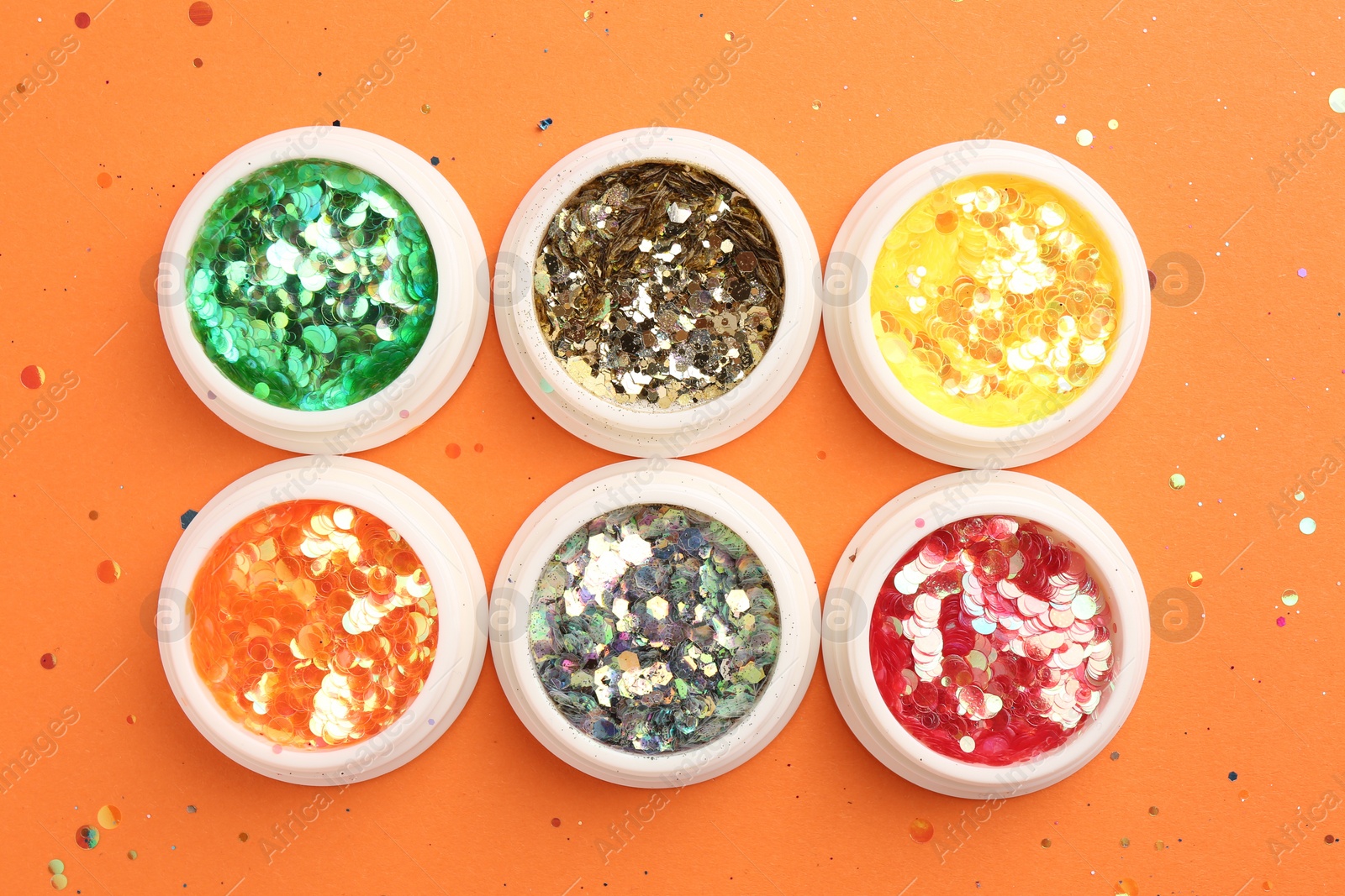 Photo of Colorful shiny glitter in jars on orange background, flat lay