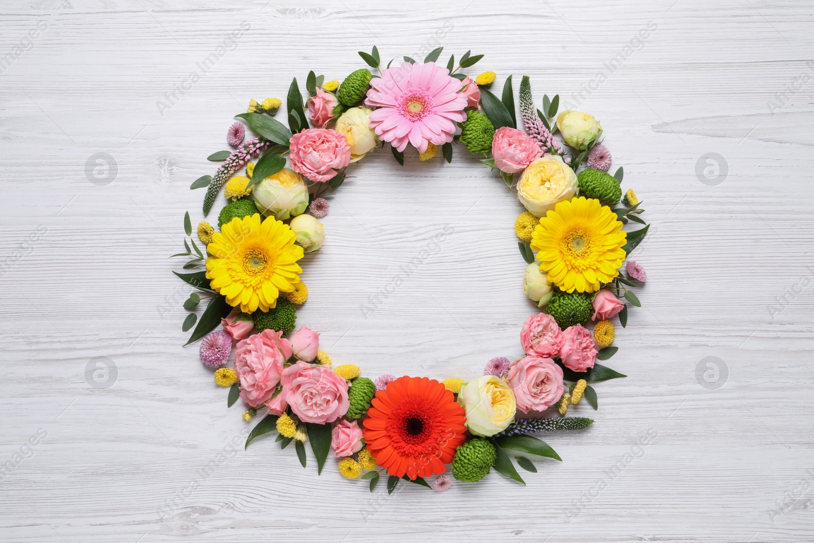 Photo of Wreath made of beautiful flowers and green leaves on white wooden background, flat lay. Space for text