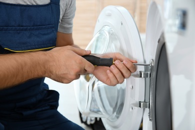 Photo of Young plumber fixing washing machine in bathroom, closeup