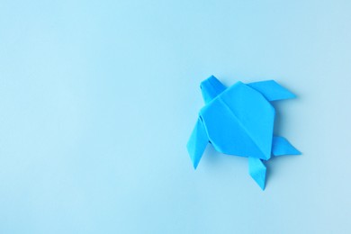 Photo of Origami art. Handmade bright paper turtle on light blue background, top view with space for text