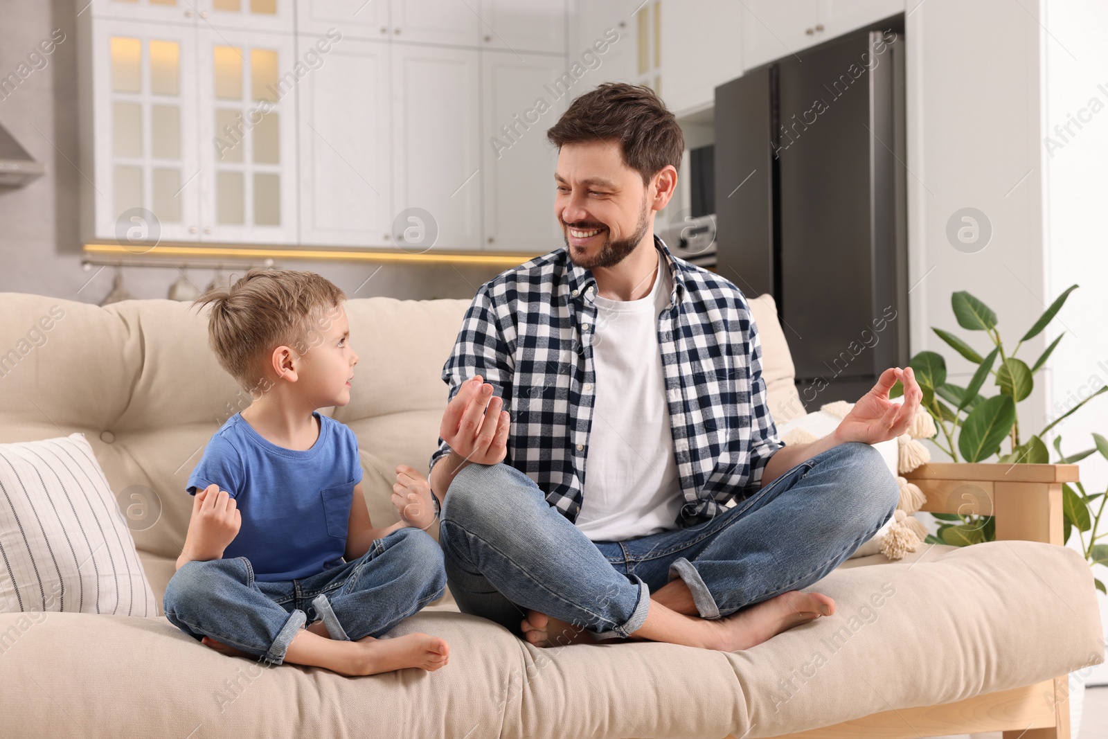 Photo of Father with son meditating together on sofa at home. Harmony and zen