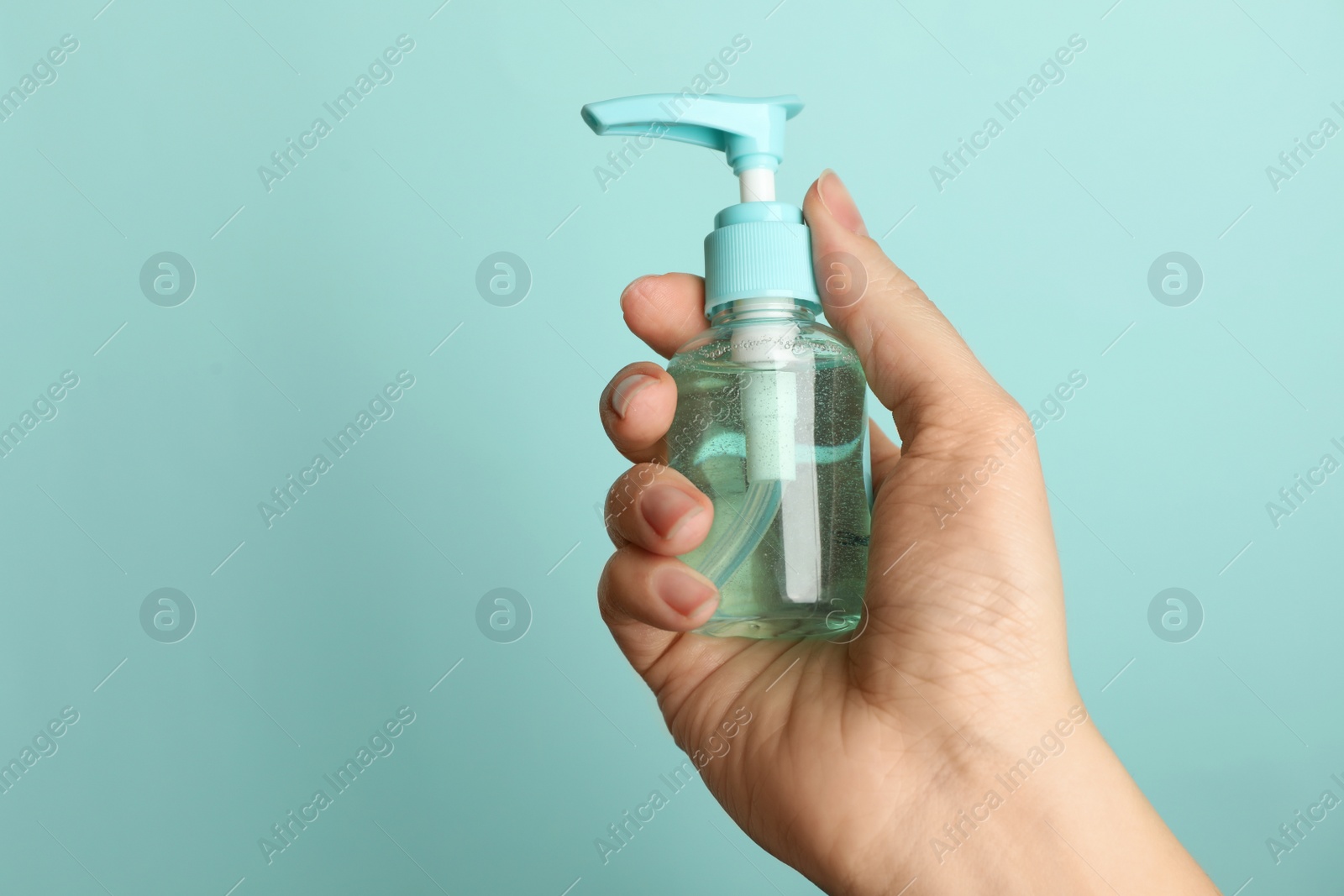 Photo of Woman holding antiseptic gel on light blue background, closeup