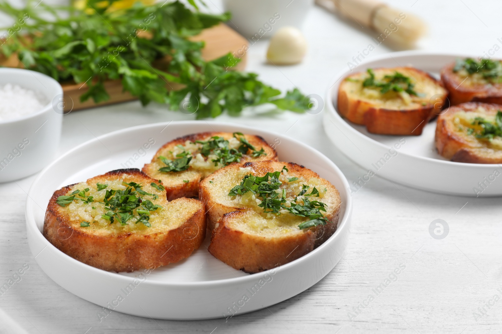 Photo of Slices of toasted bread with garlic and herb on white wooden table