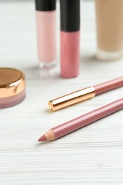 Lip pencils and other makeup products on white wooden table