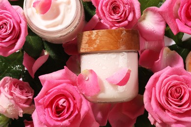 Photo of Jars of face cream among beautiful roses, top view