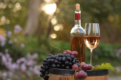 Delicious wine and ripe grapes on wooden barrel outdoors, space for text