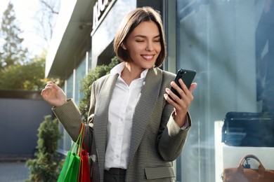 Photo of Special Promotion. Happy young woman with shopping bags and smartphone on city street