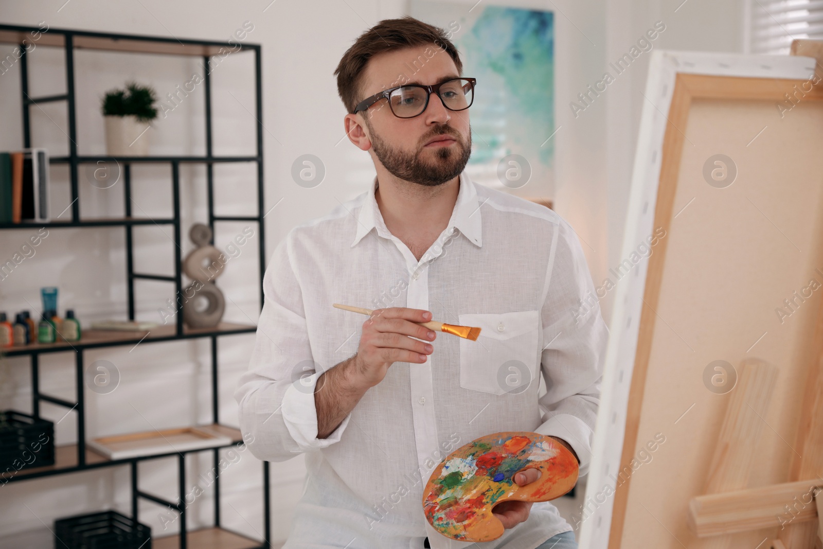 Photo of Young man painting on easel with brush in artist studio