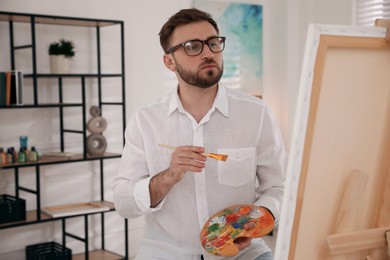 Young man painting on easel with brush in artist studio