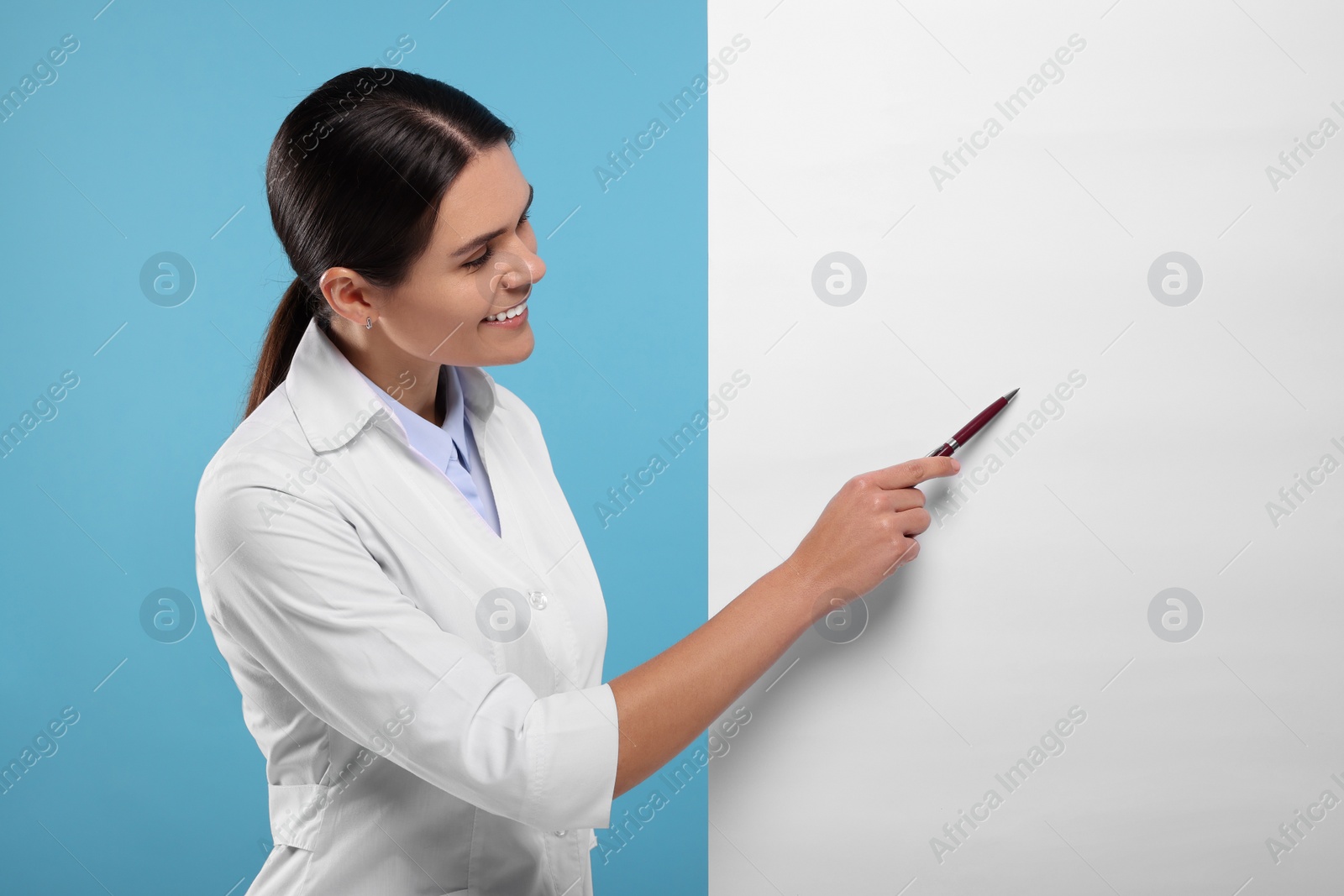 Photo of Ophthalmologist pointing at blank banner on light blue background, space for text