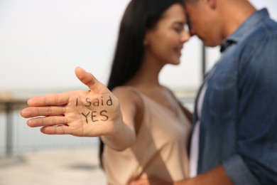 Woman with text I SAID YES written on palm and her boyfriend after engagement outdoors, focus on hand