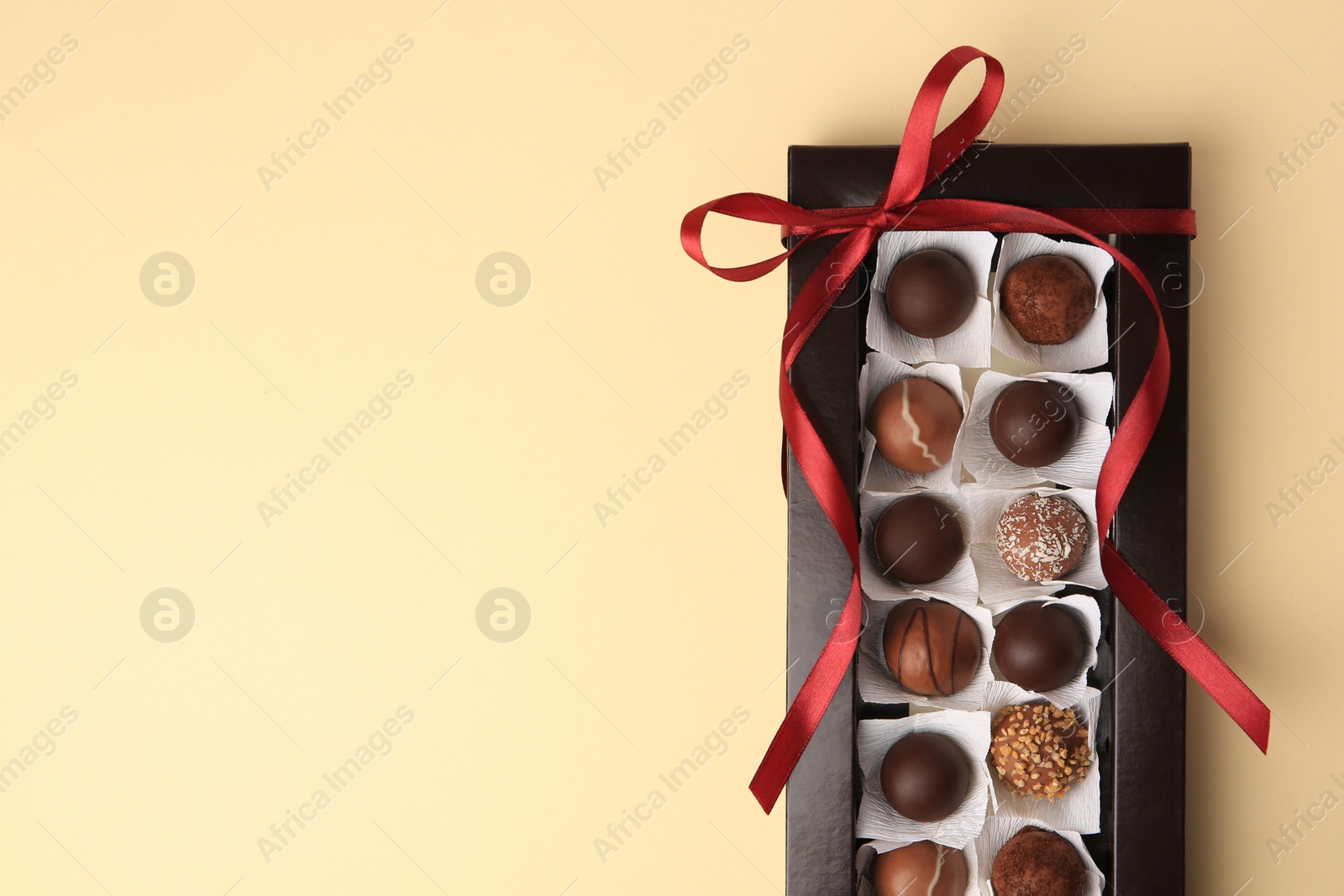 Photo of Box with delicious chocolate candies on beige table, top view. Space for text