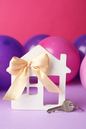 Photo of House model with bow, key and colorful balloons on violet table. Housewarming party