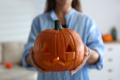 Photo of Woman holding pumpkin jack o'lantern indoors, closeup. Halloween celebration