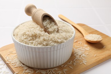 Photo of Raw basmati rice in bowl, scoop and spoon on white table