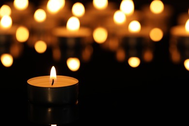 Burning candle on surface in darkness, closeup. Space for text