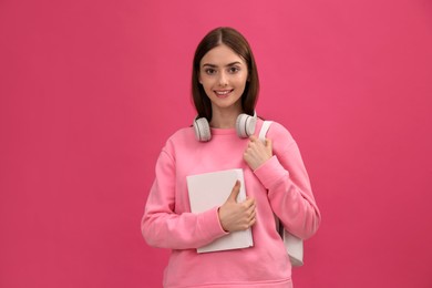 Teenage student with book, headphones and backpack on pink background