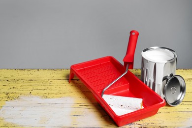 Photo of Can of paint, tray with roller on yellow wooden table. Space for text