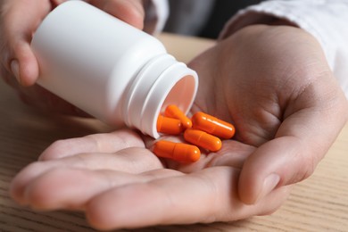 Photo of Man pouring pills from bottle at wooden table, closeup