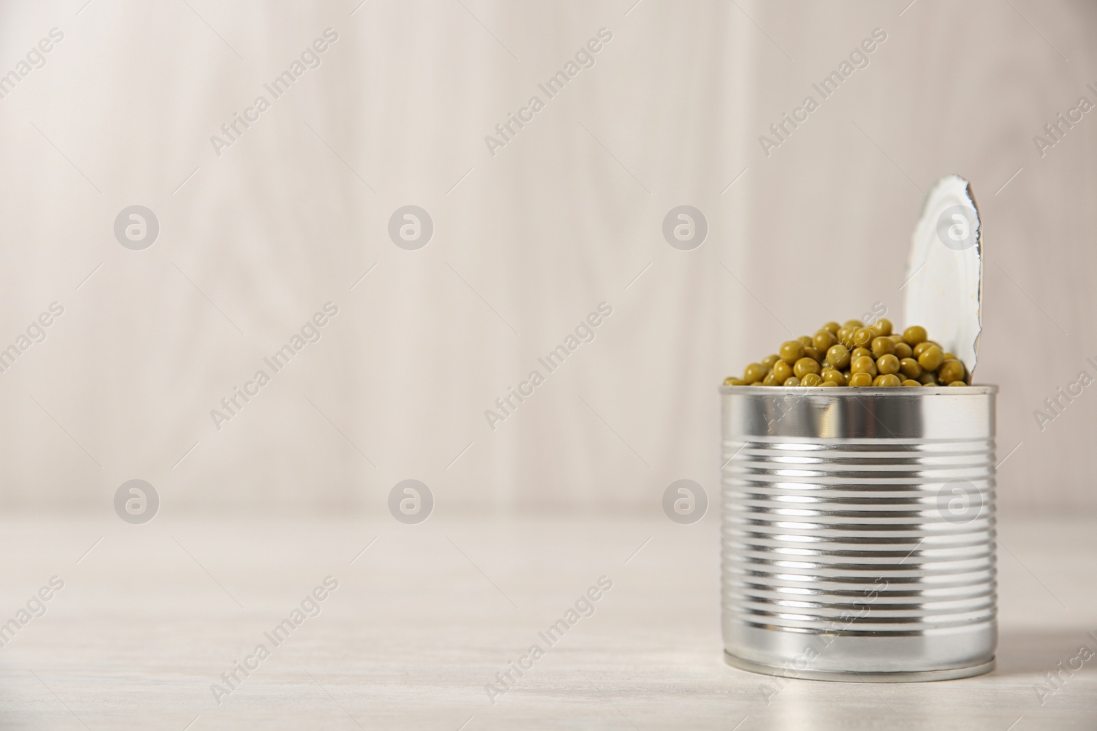 Photo of Open tin can of green peas on light table, space for text
