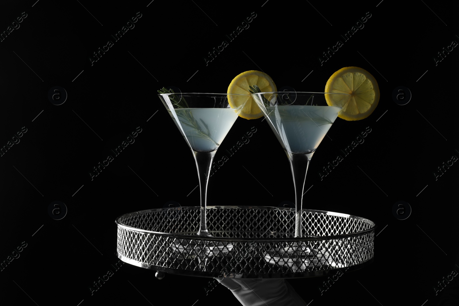 Photo of Waiter holding elegant tray with martini glasses of fresh cocktail against black background, closeup