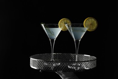 Photo of Waiter holding elegant tray with martini glasses of fresh cocktail against black background, closeup