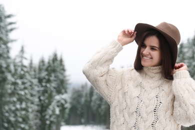 Photo of Young woman in warm sweater near snowy forest, space for text. Winter vacation