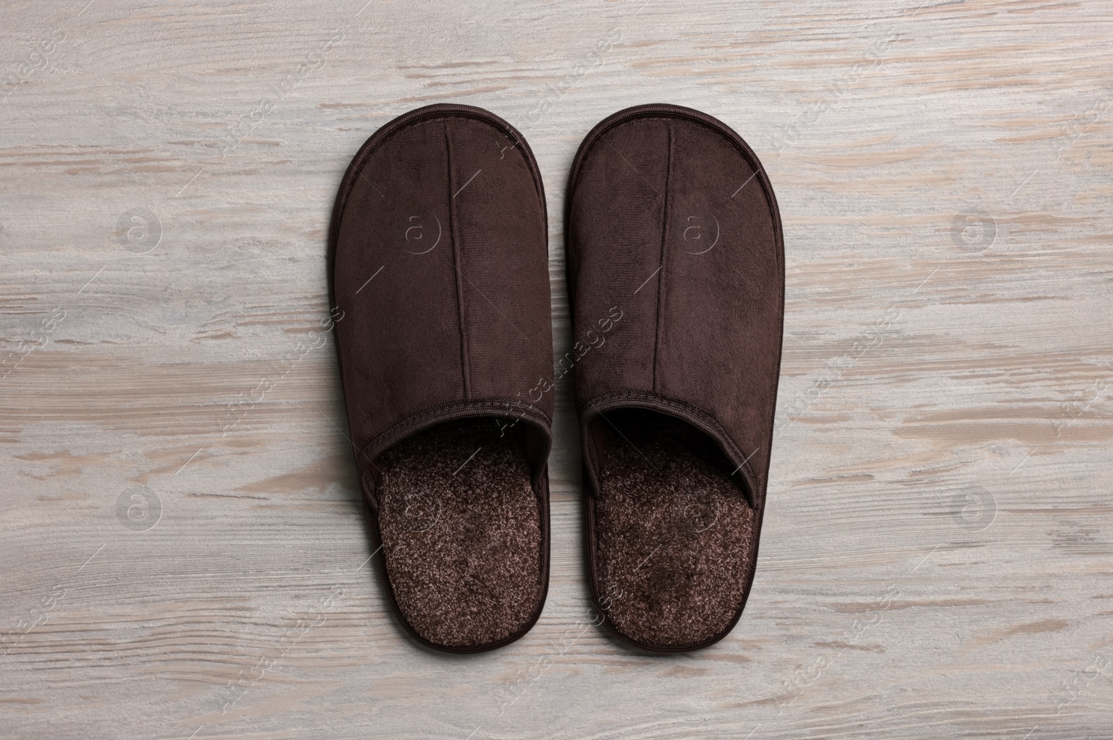 Photo of Pair of brown slippers on white wooden floor, top view
