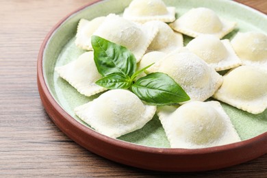Uncooked ravioli and basil on wooden table, closeup
