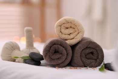 Spa stones, rolled towels and herbal bags on massage table indoors, closeup