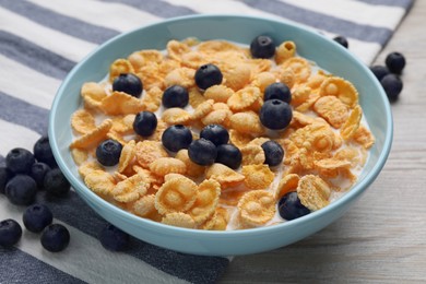 Photo of Bowl of tasty crispy corn flakes with milk and blueberries on wooden table, closeup